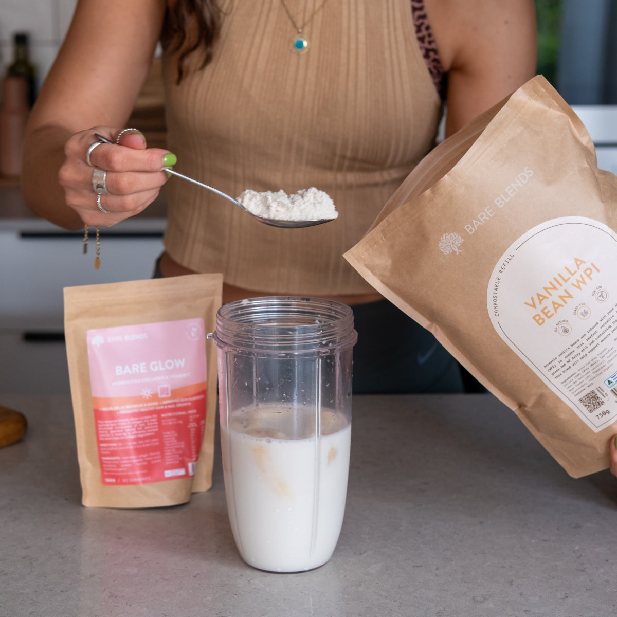 Spoonful of Bare Blends Vanilla Bean WPI being added to a smoothie with Bare Glow