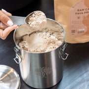 Scoop of Bare Blends Raw Cacao Fava Protein powder above a stainless steel canister