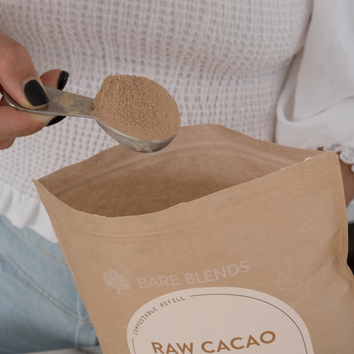 Scoop of Raw Cacao WPI protein powder held above an open Bare Blends pouch