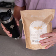 Bare Blends Vanilla Bean WPI 750g pouch held beside a black protein shaker