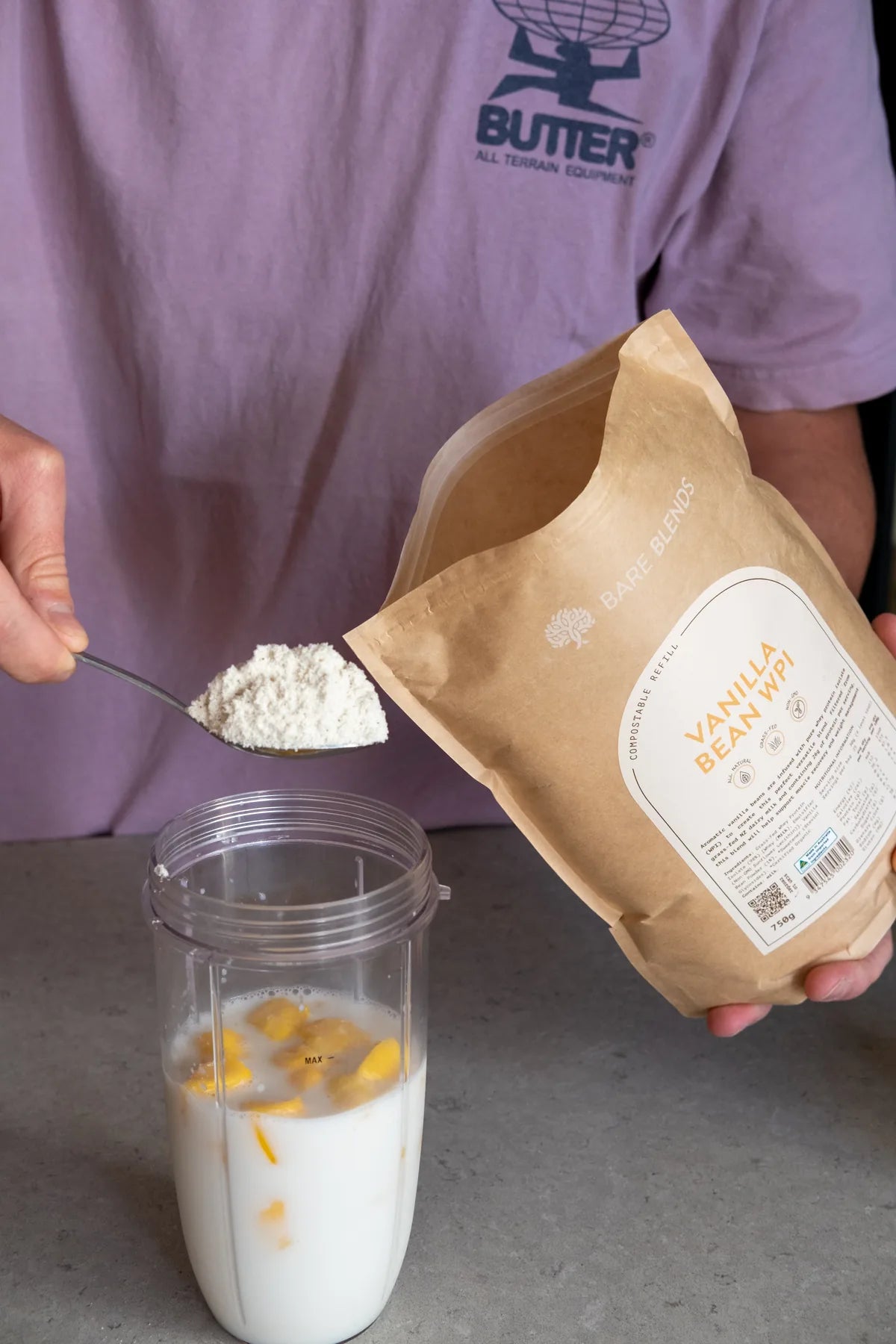 Spoonful of Bare Blends Vanilla Bean WPI beside an open pouch and smoothie blender